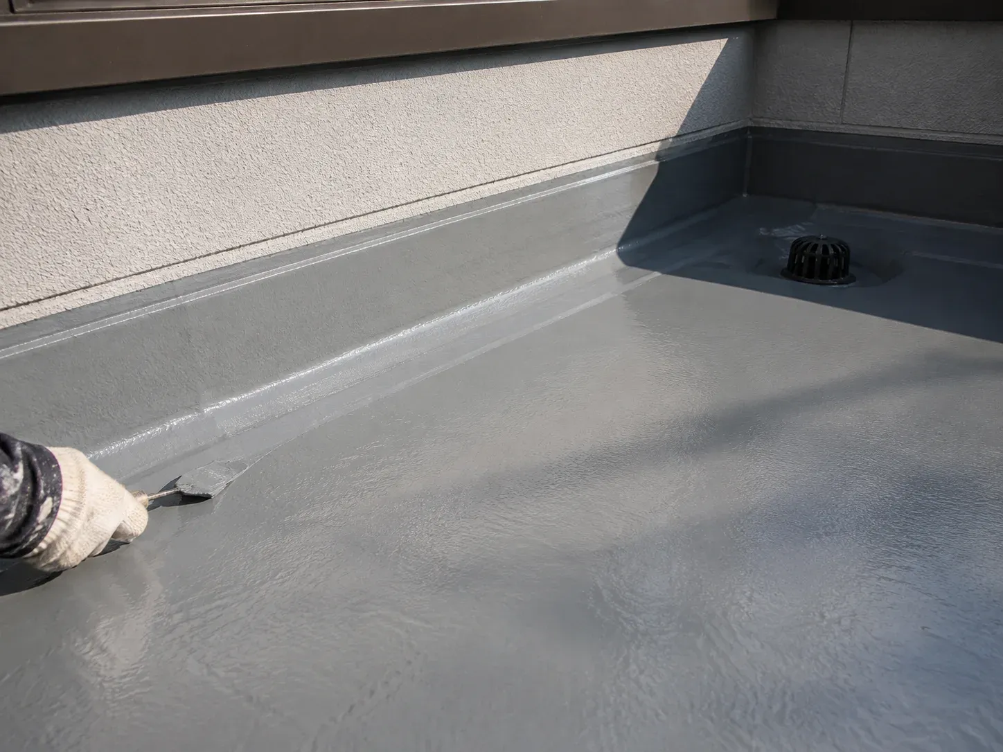 ベランダの防水施工。立ち上がりと排水ドレンに防水塗膜を仕上げる手元（イメージ）